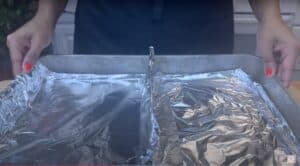 Hands holding a baking sheet lined with aluminum foil, ready for cooking.